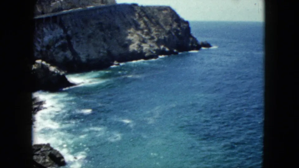 8mm film frame circa 1962 showing breaking waves at the base of a pale rocky cliff, likely along the Acapulco coast, Mexico.