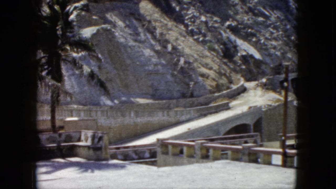 Concrete balustrade viewing area with winding cliffside road and rocky mountain, 8mm film