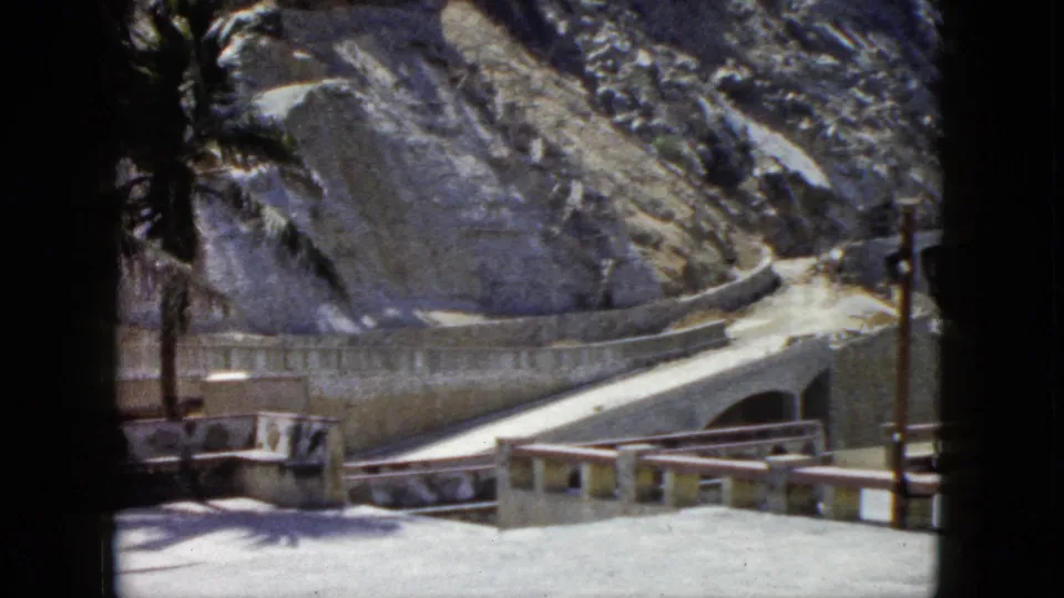 Tourist overlook with concrete balustrade, winding cliffside road, and palm trees against a rocky hillside, Acapulco, Mexico, circa 1962, 8mm film