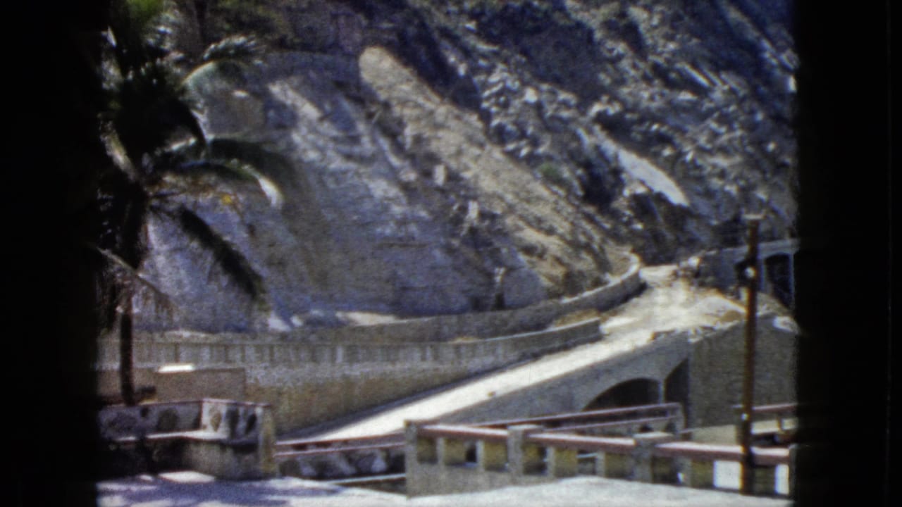 Tourist overlook with decorative balustrade, winding mountain road, and palm tree against bare rocky hillside, Acapulco, Mexico, circa 1962