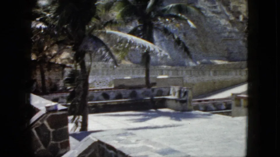 Stone-paved terrace with decorative stone wall edging and palm trees at a coastal Acapulco overlook, circa 1962; an establishing wide shot with no prominent figures.