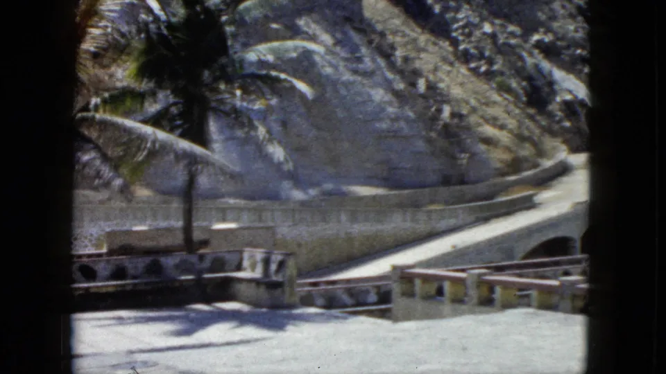 Curved stone terrace with retaining wall and winding road or path along a rocky cliffside at what appears to be an Acapulco coastal viewpoint, circa 1962.