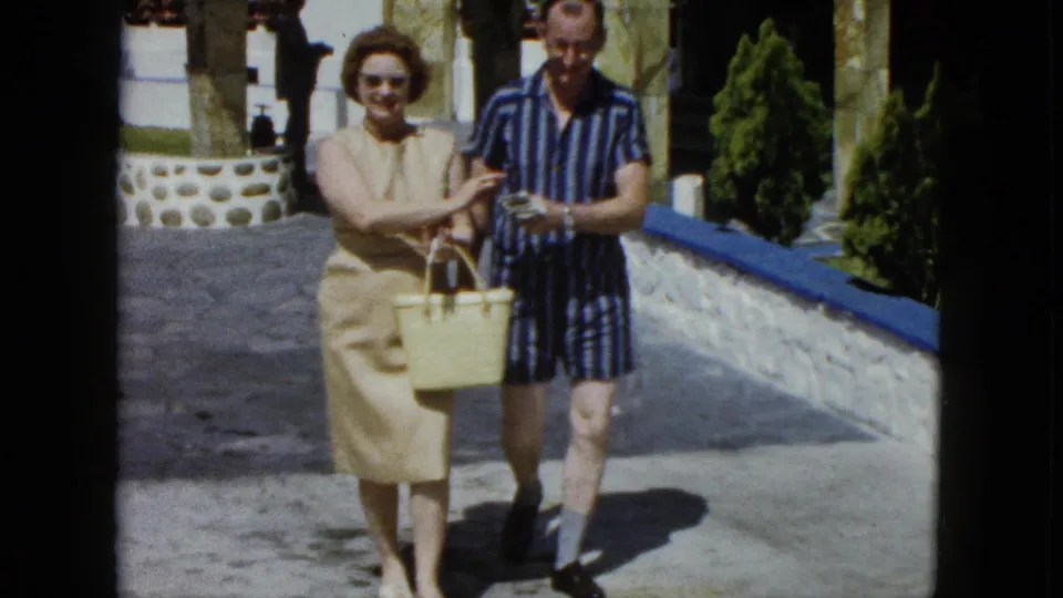 Tourist couple at an Acapulco resort, circa 1962, looking down at a yellow wicker basket and apparently handling its contents, possibly currency, shot on 8mm film.
