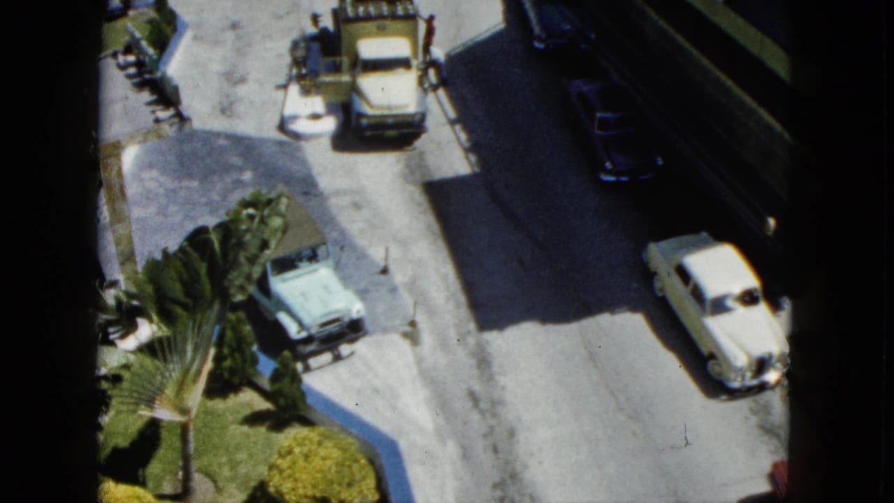 1962 Acapulco home-movie frame showing an elevated street view with mid-century cars, a utility truck, palms, and distant pedestrians.