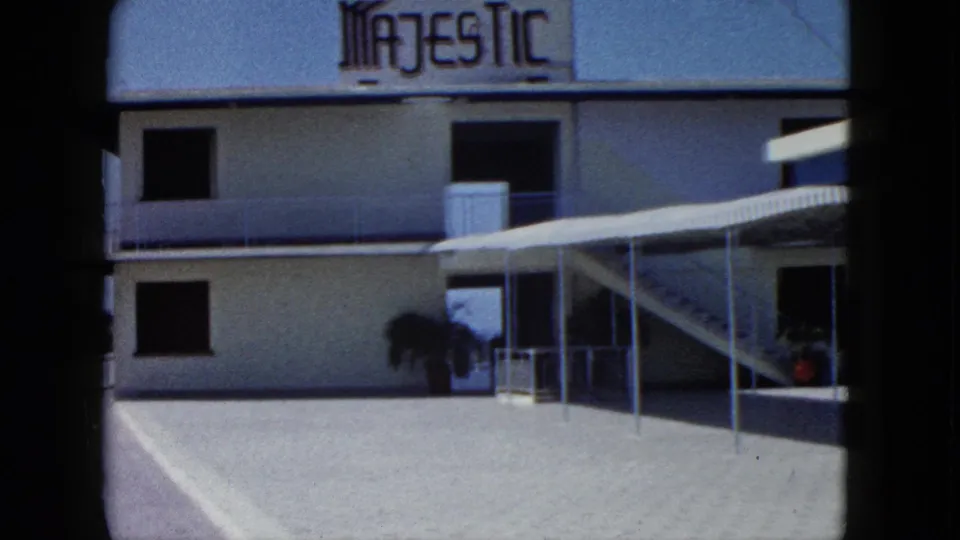 1962 Acapulco frame showing a modern building facade with the "MAJESTIC" sign, terrace railings, awning, and a potted plant.
