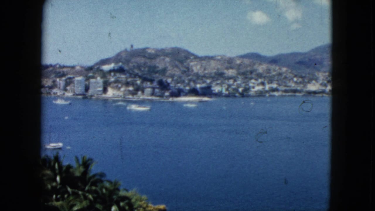 Acapulco bay seen through dark window framing, with boats, shoreline buildings, and mountains.