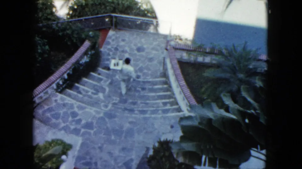 1962 Acapulco footage shows a person descending a broad stone staircase with railings, exterior walls, and tropical plants nearby.