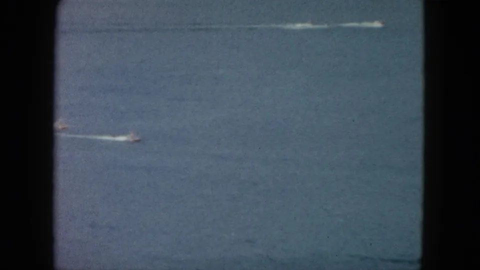 1962 Acapulco home-movie frame showing a small speedboat moving across open blue water with a pale wake behind it.