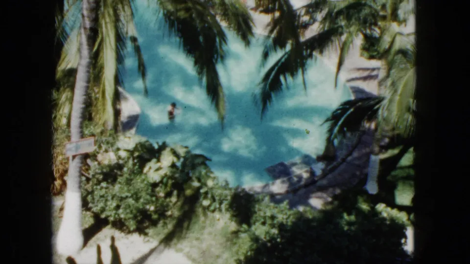 1962 Acapulco resort view from above, showing palm trees, dense landscaping, and a person swimming in a turquoise pool.