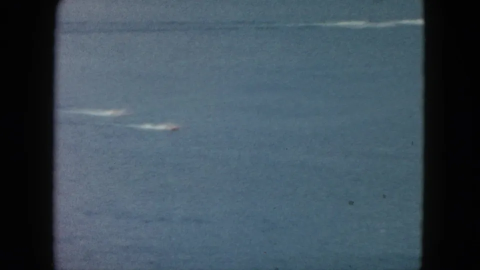 1962 Acapulco frame with two small speedboats and long white wakes visible against faded blue ocean water.