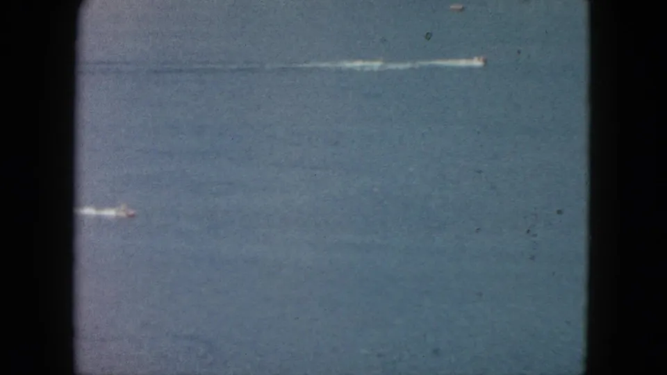 1962 Acapulco 8mm frame showing a lower-left speedboat and a long wake from another boat across open ocean.