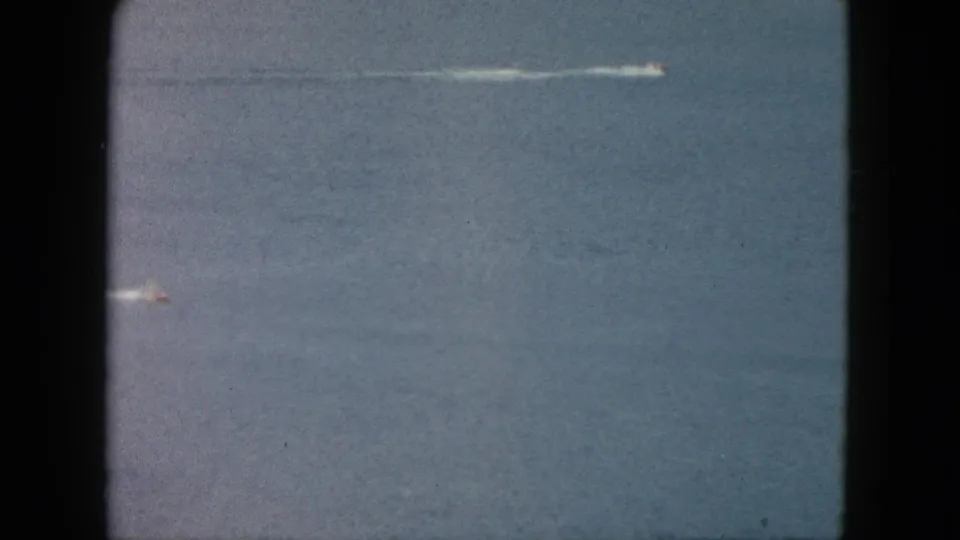 1962 Acapulco frame with two distant speedboats on blue ocean, each leaving a white trail in the water.