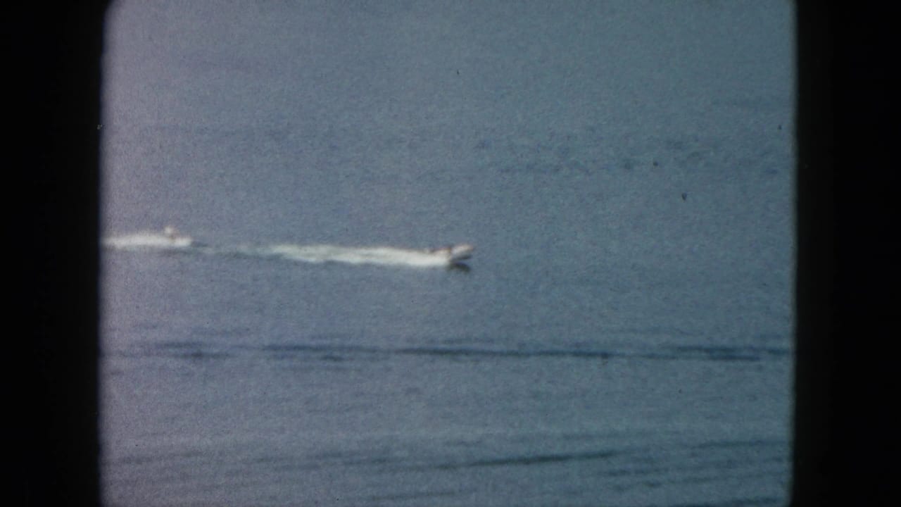 1962 Acapulco home-movie frame showing a distant motorboat moving across turquoise ocean water with a white wake.