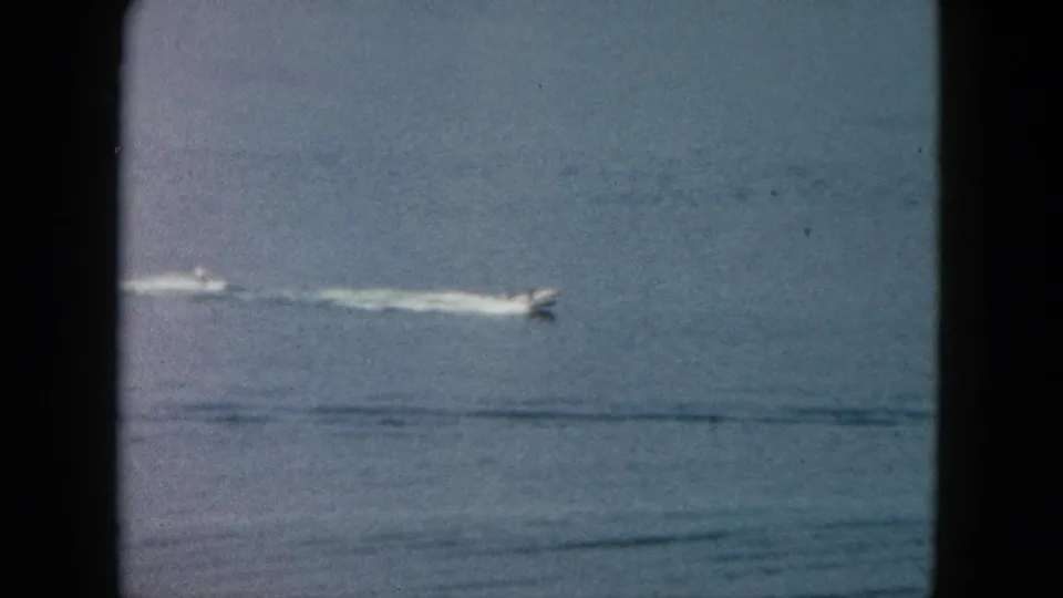 1962 Acapulco home-movie frame showing a distant motorboat moving across turquoise ocean water with a white wake.