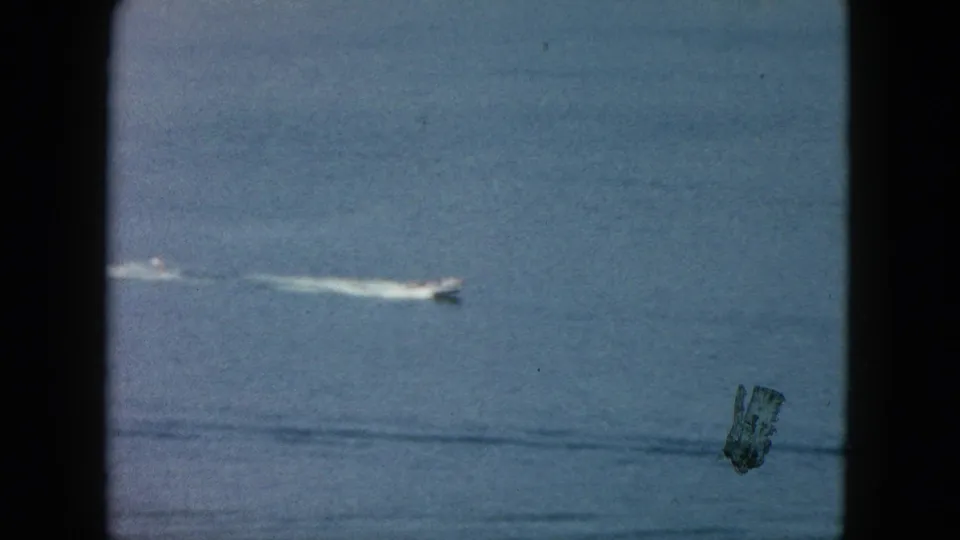 1962 Acapulco home-movie frame showing a small white speedboat moving across blue ocean water behind dark vertical framing.