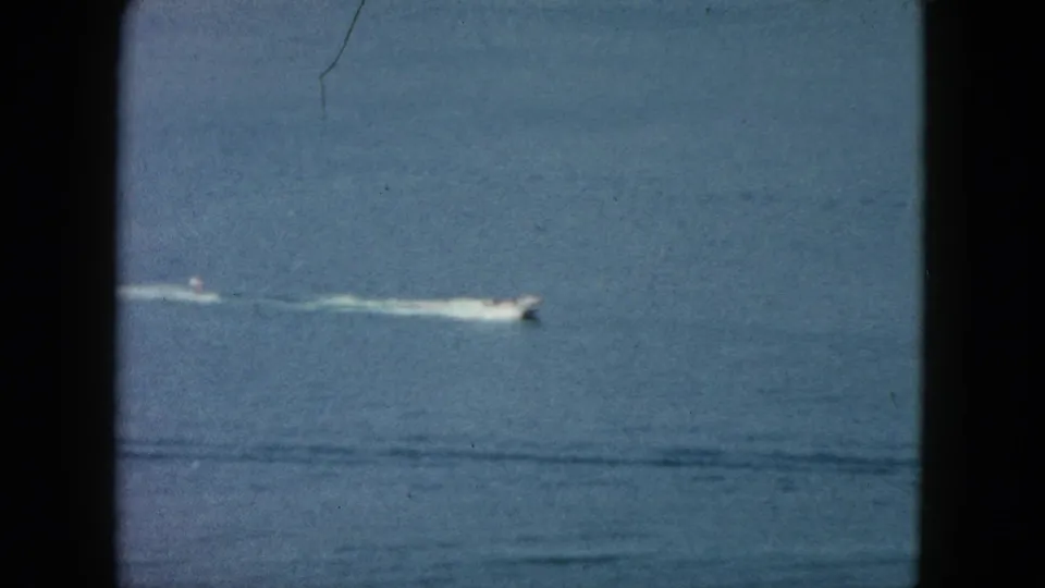 1962 Acapulco 8mm frame with a distant white speedboat racing across open blue water and leaving a long white wake.