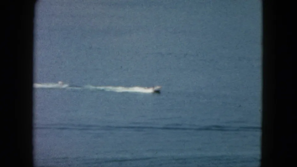Vintage 8mm Acapulco frame showing a distant white speedboat low in the composition with wake across the ocean surface.