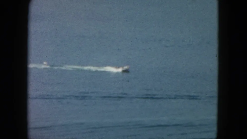1962 Acapulco home-movie still of a small speedboat moving across the ocean, partly framed by a dark vertical foreground edge.