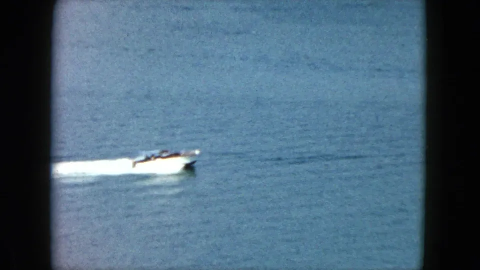 1962 Acapulco home-movie frame of a small white speedboat crossing calm blue water with passengers faintly visible.