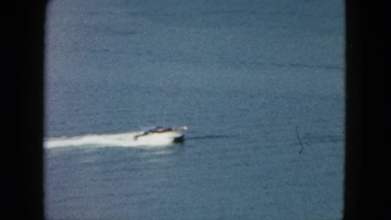 Small speedboat in Acapulco water, seen through dark 8mm frame edges with a long wake trailing behind.