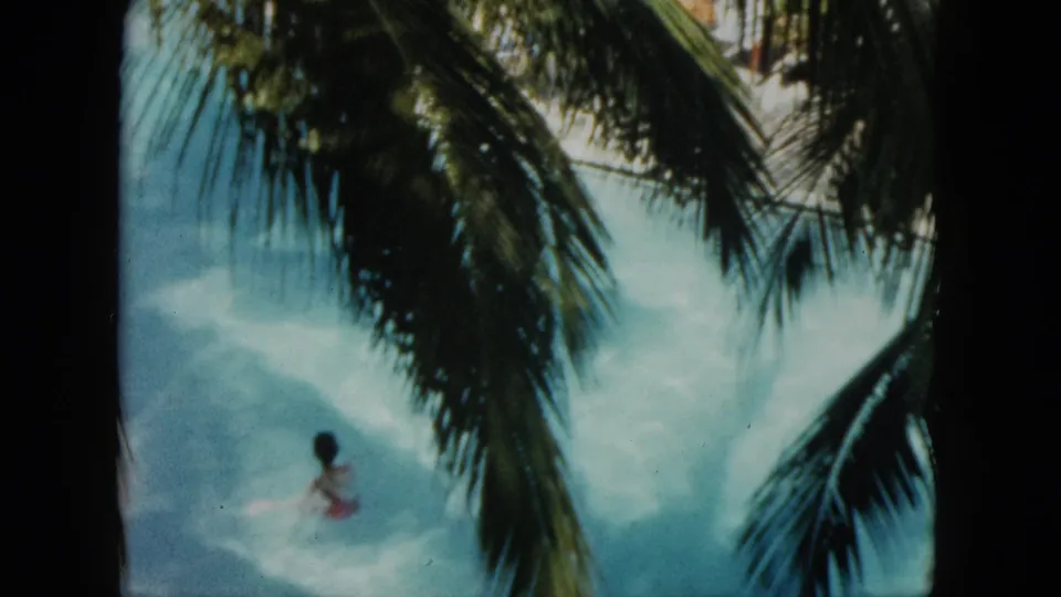 A swimmer moves through bright blue water below overlapping palm fronds in a 1962 Acapulco 8mm vacation frame.