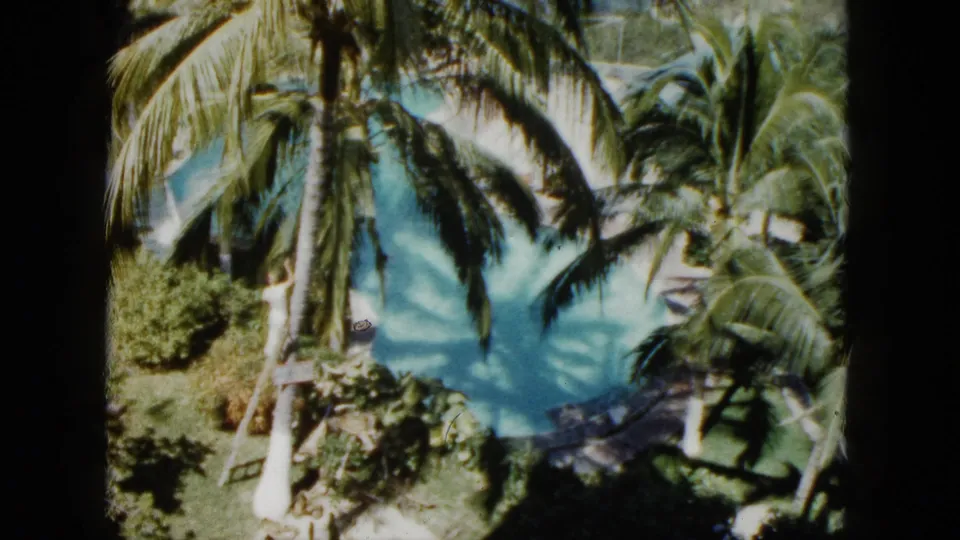 Acapulco home-movie frame from 1962 showing the pool from above, shaded by palm leaves with a small swimmer-like figure in the water.