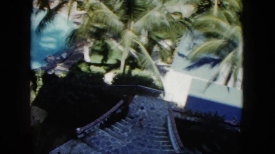 1962 Acapulco resort grounds with stone steps, curved path, palms, and pool water in a handheld 8mm frame.