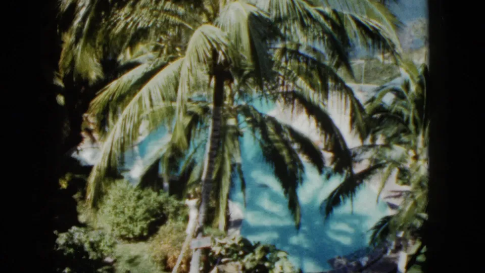 1962 Acapulco home-movie frame showing palm trees and blue-green pool water with a soft, dark 8mm border.