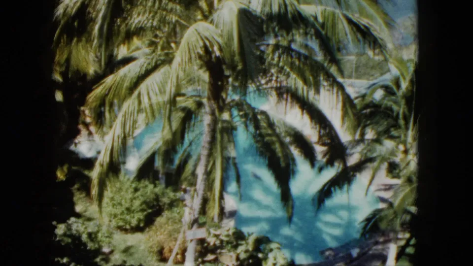 A slightly shifted 8mm frame shows tall palms, heavy fronds, and blue pool water at an Acapulco resort setting.