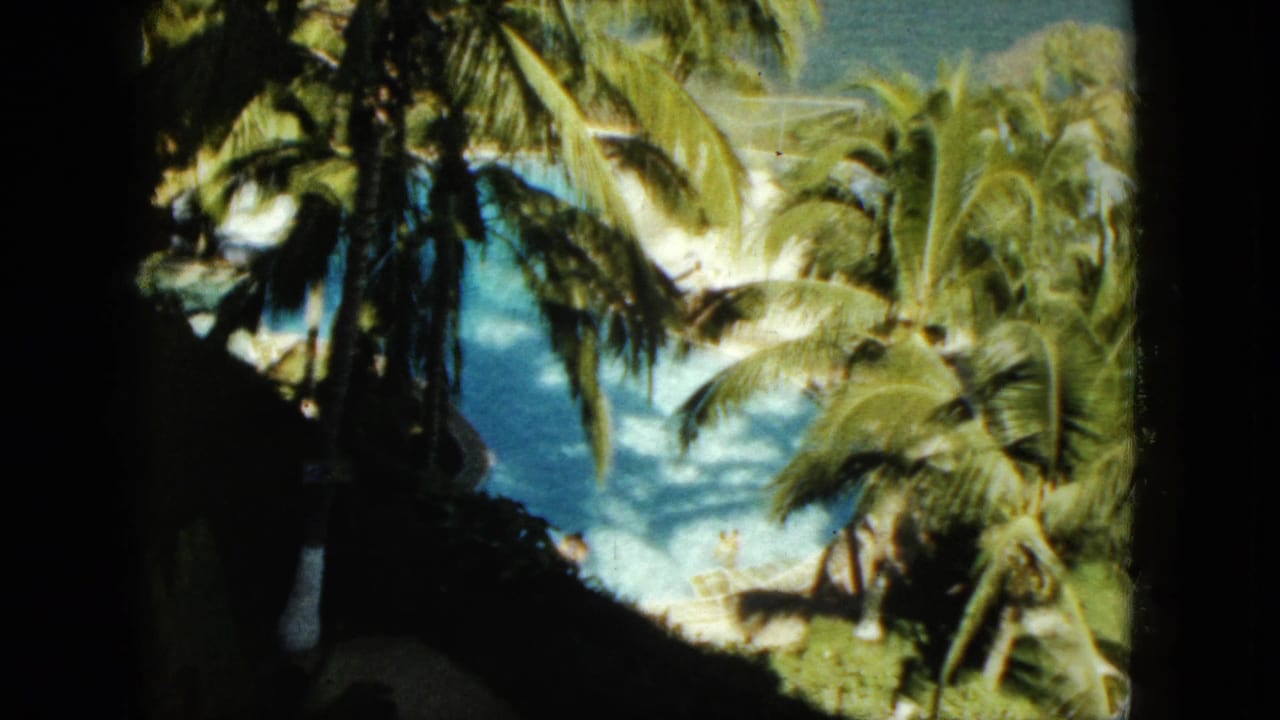 1962 Acapulco home-movie frame of palms overlooking a blue swimming pool and water beyond, partly obscured by dark foreground shade.