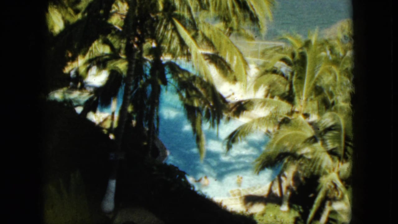 1962 Acapulco resort view with palm trees, a blue swimming pool, and tiny swimmers seen from an elevated home-movie angle.