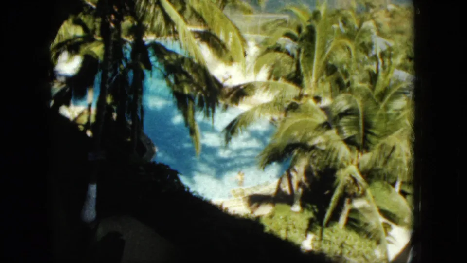 Coconut palms and bright pool water dominate this 1962 Acapulco vacation view, with a dark frame at left.