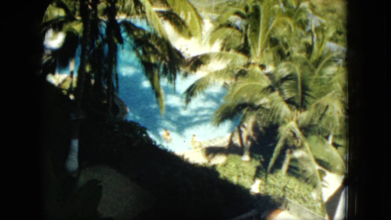 High-angle 1962 Acapulco resort view showing a blue pool partly obscured by palms and dark foreground shadows.
