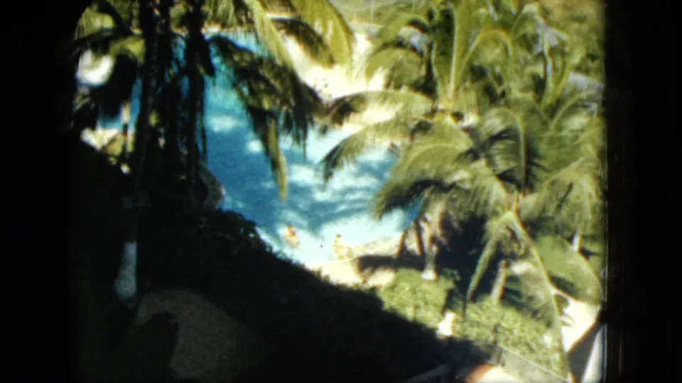 High-angle 1962 Acapulco resort view showing a blue pool partly obscured by palms and dark foreground shadows.
