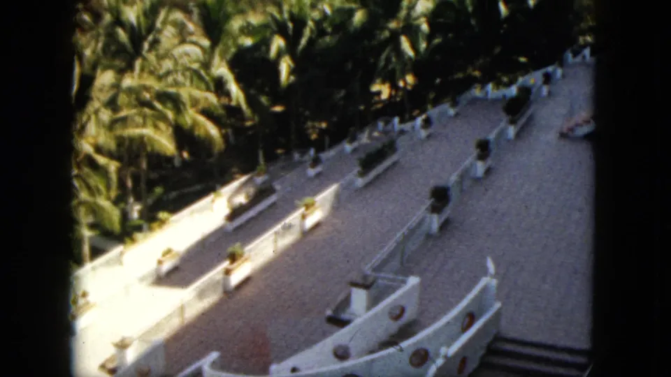 1962 Acapulco frame with a sunlit white terrace, curved walls, round openings, steps, and palms behind the resort structure.