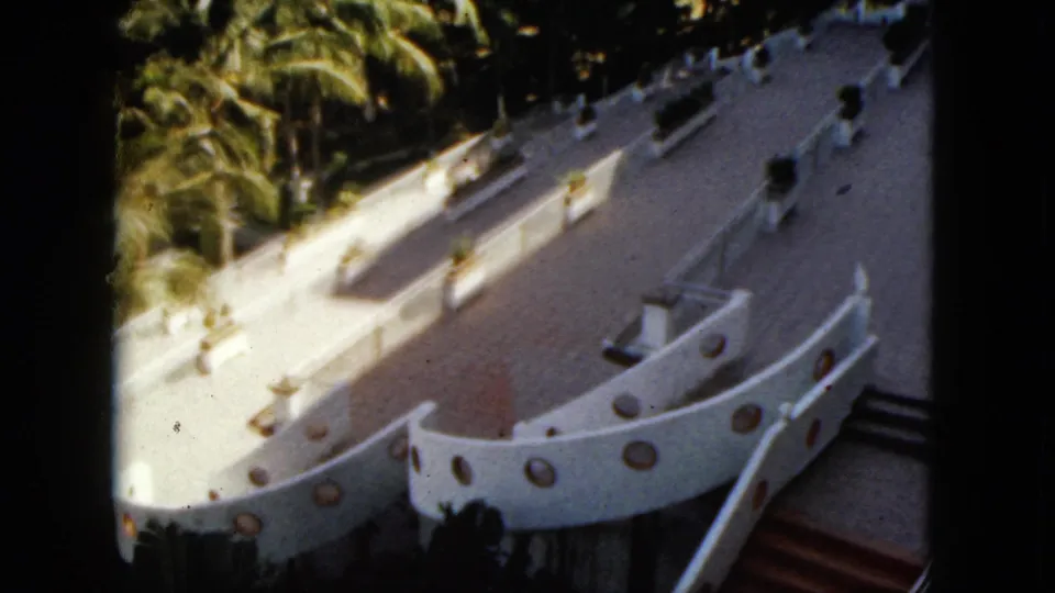 1962 Acapulco home-movie still showing the curved white resort structure, round porthole-like details, stairs, palms, and tiled terrace.