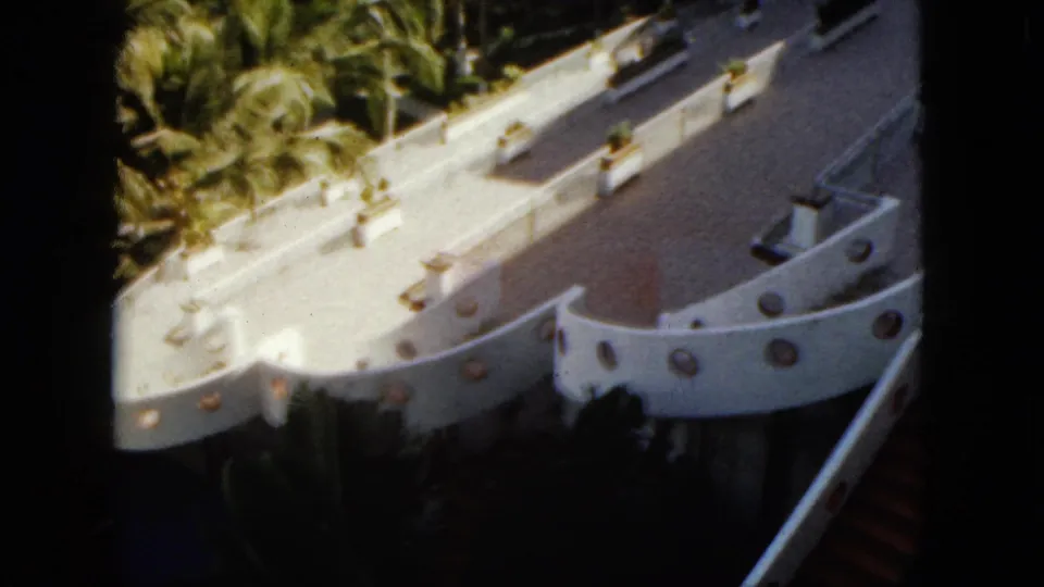 1962 Acapulco frame of the white boat-shaped resort feature with circular wall details, tiled surfaces, steps, and surrounding palms.