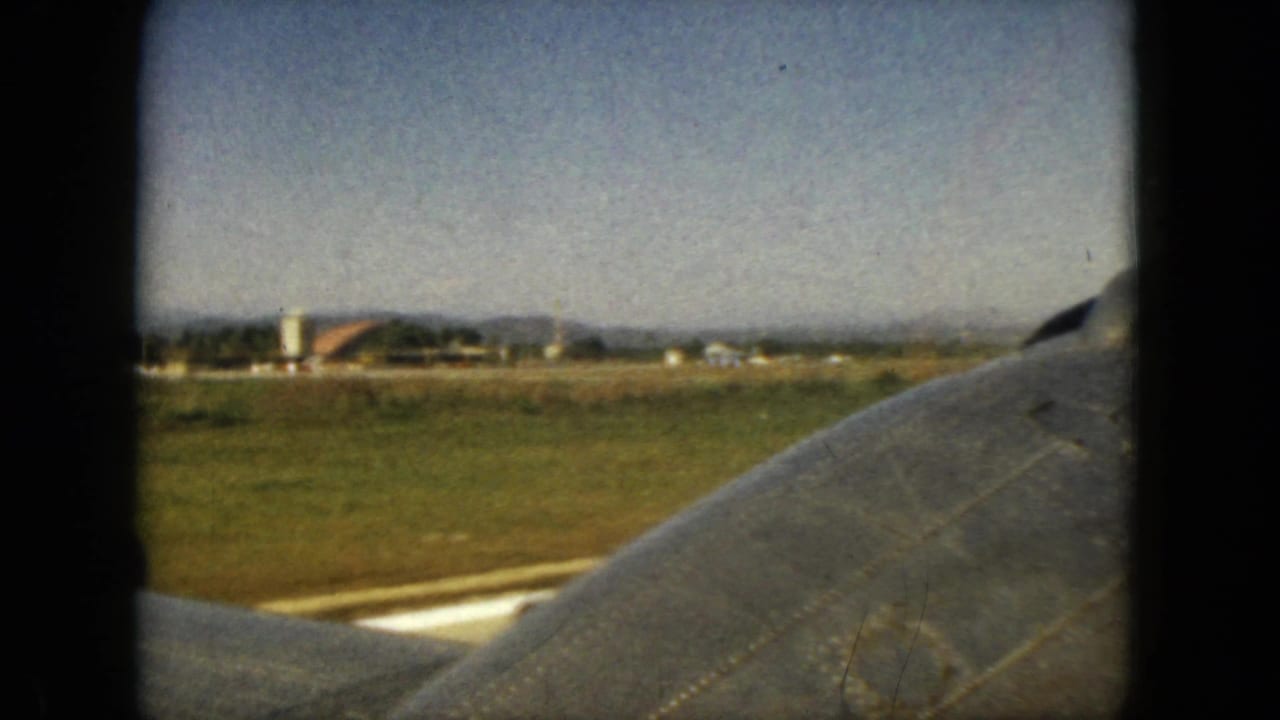 Airplane wing and distant buildings visible through a plane window.