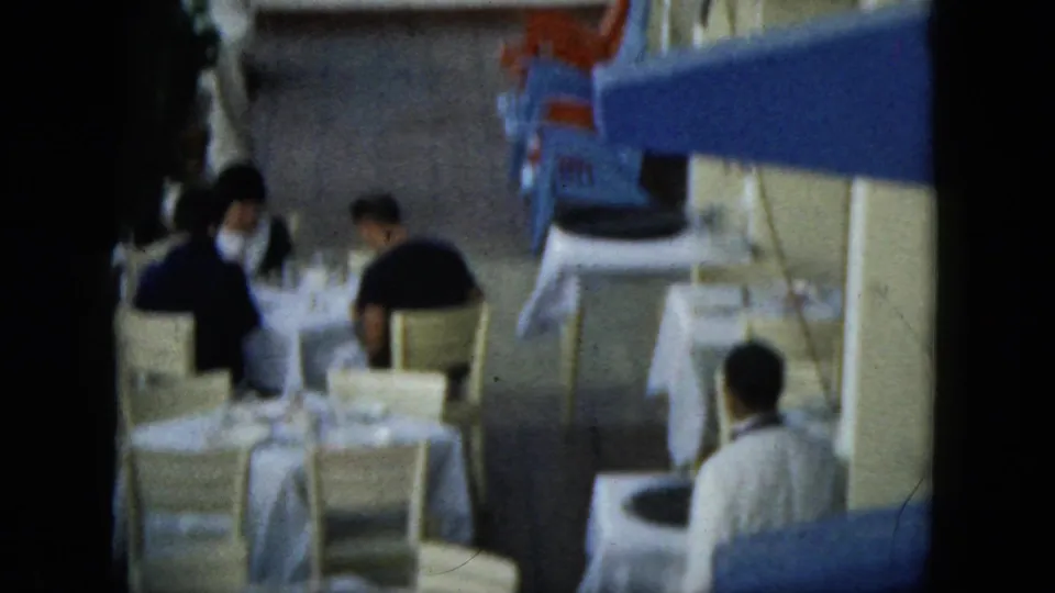 In the Acapulco travel footage, several diners sit at white-covered outdoor tables near a blue awning and pale building wall.
