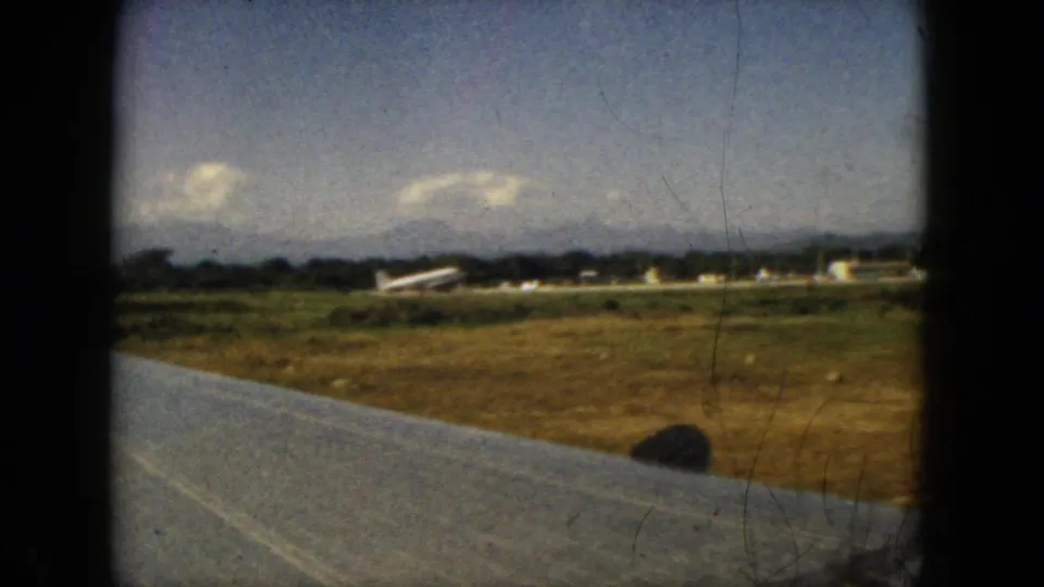 1962 Acapulco airport view from an airplane window, with wing foreground, grassy field, small aircraft, and low buildings.