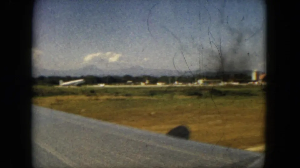 Passenger-window frame from Acapulco, Mexico, with the airplane wing crossing the foreground and airport buildings beyond a grassy runway.