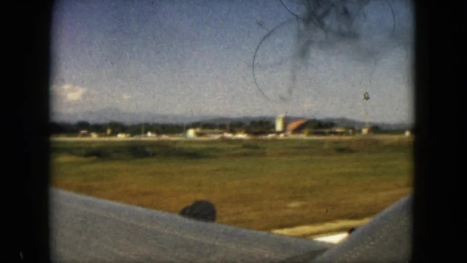 1962 Acapulco airplane-window view showing the wing in foreground, runway grass, airport structures, distant hills, and scattered clouds.