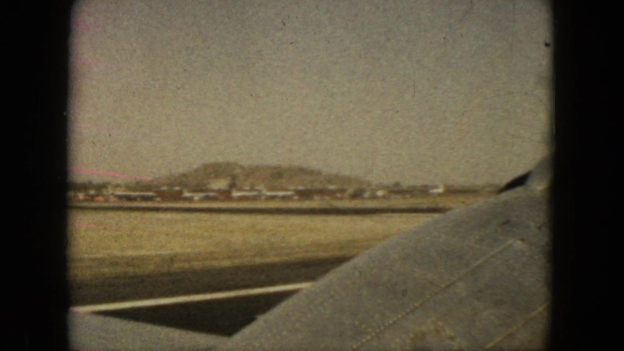 1962 Acapulco airplane-window view with the wing in foreground and low buildings and hills beyond the ground strip.