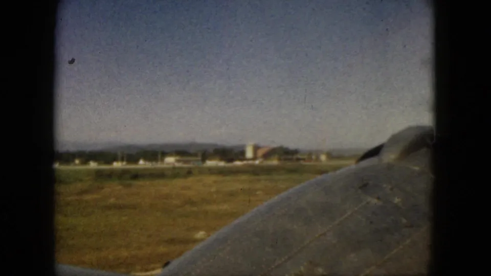 1962 Acapulco 8mm frame showing an airplane wing above fields, scattered buildings, and distant hazy mountains.