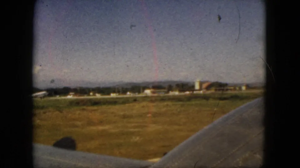 1962 Acapulco airplane-window frame with sunlit fields, distant buildings, hills, and the aircraft wing in foreground.