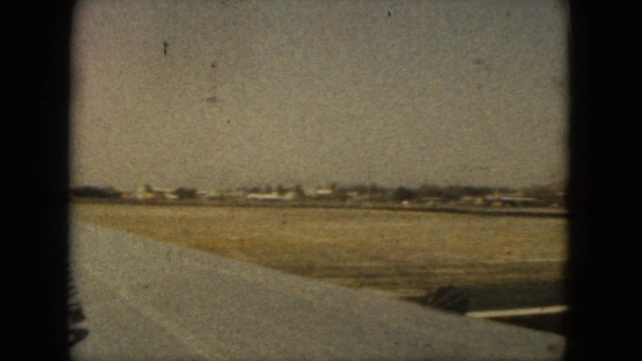 Runway and airport grounds seen from an airplane window with low buildings in the distance.