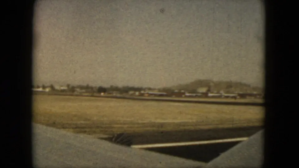 1962 Acapulco runway view over the aircraft wing, with low airport structures and hills visible through faded 8mm color.