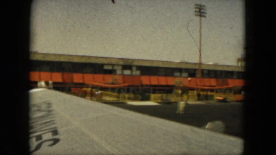 End frame of the 1962 Acapulco airplane-window view, with the wing, terminal building, orange panels, and tarmac visible.