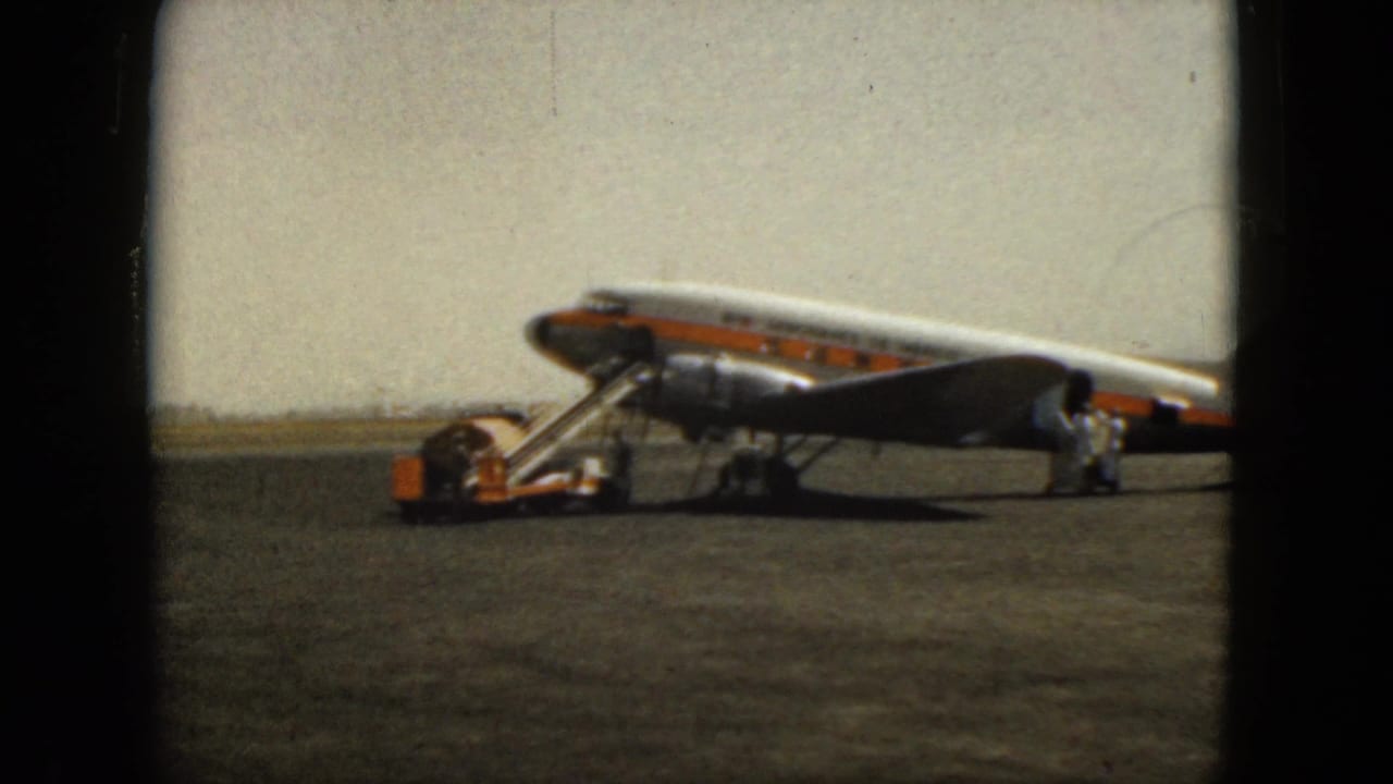 Propeller passenger plane on a tarmac with boarding stairs and ground crew nearby.