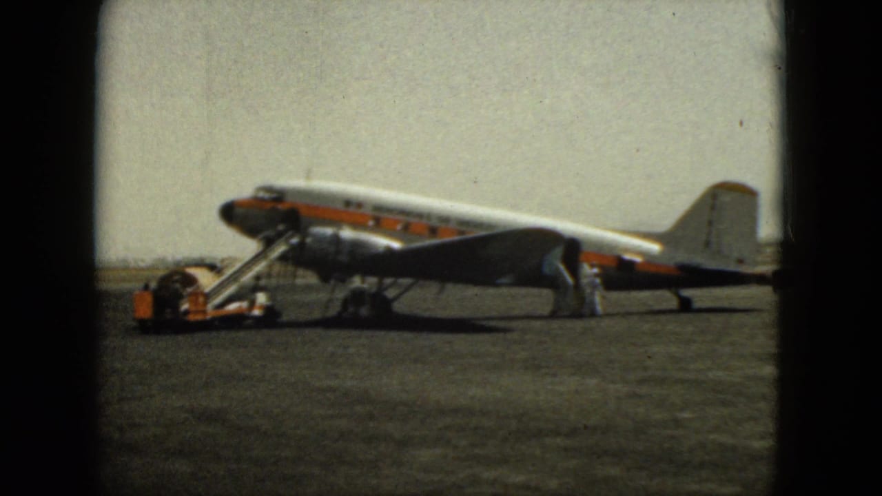 Propeller aircraft with boarding stairs connected and people standing near the rear doorway.